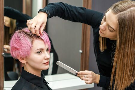 Hairdresser checking short pink hairstyle of young woman in hair salon.の写真素材