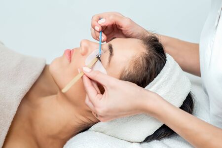 Cosmetologist's hand extends eyelashes with the help of a cotton bud.
