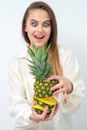 Surprised facial expression of beautiful young woman holding pineapple in section, close up.の写真素材