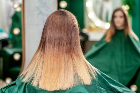 Back view of young woman with new hairstyle is sitting in front of the mirror in the hair salon.の写真素材