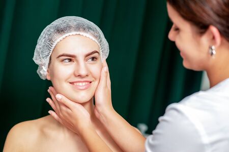 Hands of beautician touching face skin of smiling young woman.