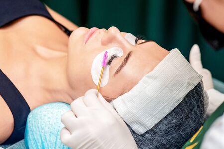 Cosmetologist combs eyelashes with eyelash brush during eyelash extension procedure in beauty salon.の写真素材
