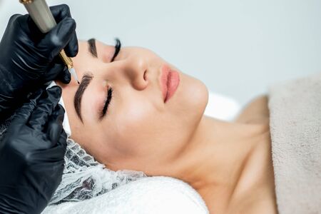Permanent make up on eyebrows of young woman by professional cosmetologist close up.の写真素材