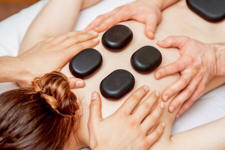 Hands of massage therapists doing back massage while hot stones on back of woman close up in spa.の写真素材