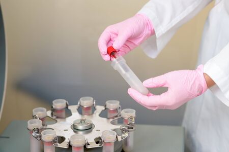 Test tube of blood in hand of doctor on centrifuge machine in medical clinic, analysis by coronavirus.の写真素材