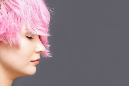Woman with pink hairstyle stands with closed eyes side view on gray background with copy space.の写真素材