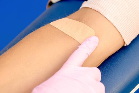 Doctor in rubber protective gloves glues an adhesive plaster on arm after blood sampling.