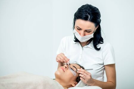 Cosmetologist is doing eyelash extension procedure of patient on white background, copy space.の写真素材