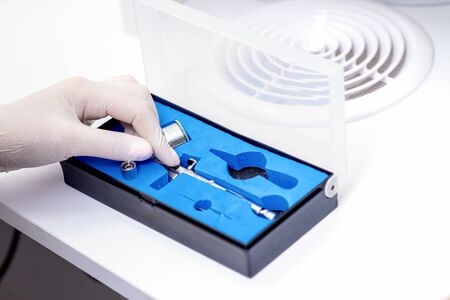 Manicure master hand is taking out airbrush tool for nails wearing white gloves from the box.