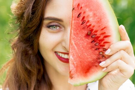 Portrait of a beautiful smiling woman is holding slice of watermelon covering half part of face, close up.の写真素材