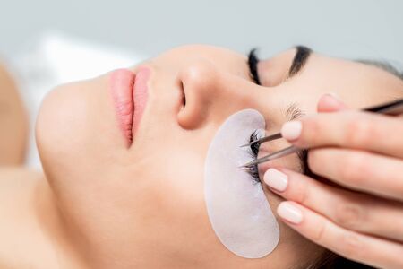 Cosmetologist hand is separating eyelashes with tweezers on eye of woman during eyelash extension procedure.の写真素材