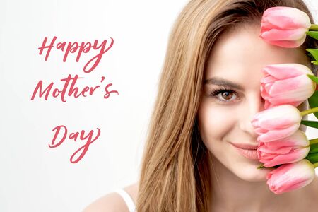 Happy Mother's Day pink text sign and portrait of smiling young woman with pink tulips on white background. Greeting card with woman and inscription Happy Mother's Day.の写真素材