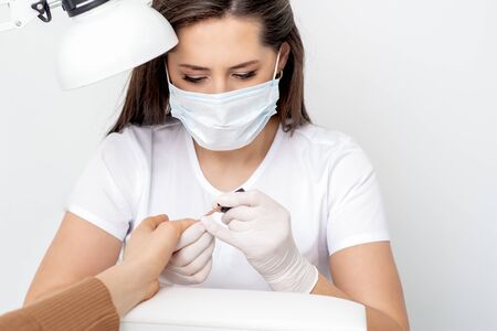 Manicurist wearing protective mask painting female nails with nail polish in manicure salon.の写真素材