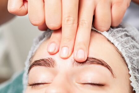 Beautiful woman receiving forehead massage by fingers of cosmetologist, close-up.の写真素材