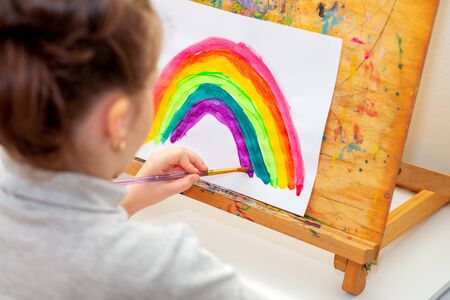 Child is drawing rainbow with watercolors on the sheet of paper on the easel. Creativity concept.の写真素材