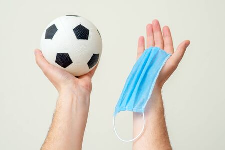 Soccer ball and medical mask in man hands up on white background.の写真素材