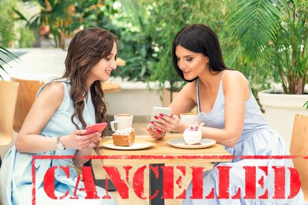 Word CANCELLED on background of two young women in the cafe outdoors. Coronavirus quarantine. Closed...