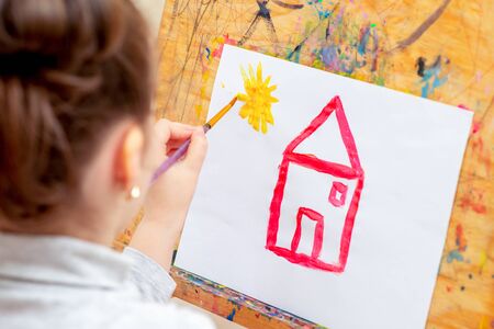 Child is drawing house with watercolors on the easel.の写真素材