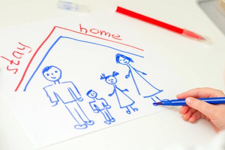 Child is drawing happy family with words Stay Home on white sheet of paper at home. Children creativity.の写真素材