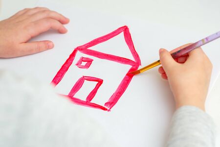 Closeup of hands of child drawing red house on white sheet of paper. Children's creativity concept.の写真素材