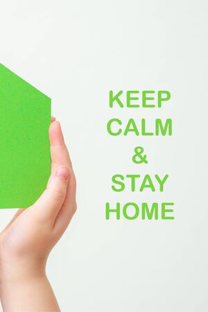 Children's hands holding a green paper house with words Stay Home on white background. Stay home concept.の写真素材