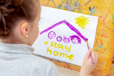 Child is drawing picture of family sketch under roof and words Stay Home with watercolors on easel...
