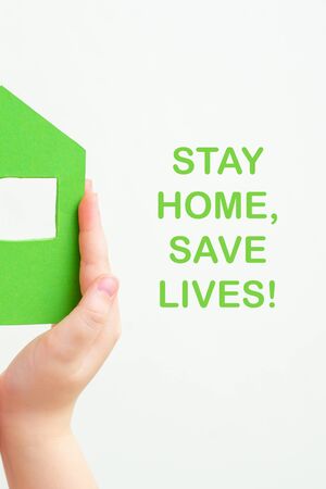 Children's hands holding a half of paper green house with words Stay Home, Save Lives on white background. Stay home concept.の写真素材