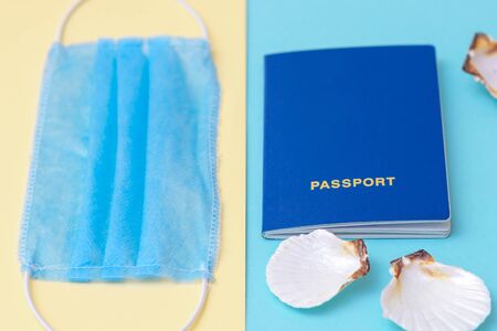 Closeup of travel still life with a passport, medical mask and seashells on a blue and yellow background. Travel concept during coronavirus. Selective focus.の写真素材