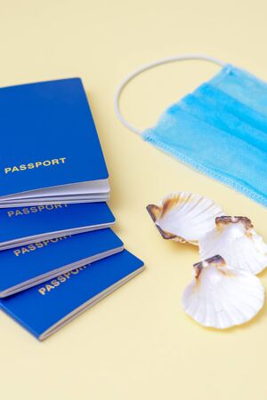 Closeup vertical image of four passports, medical mask and seashells on a blue and yellow background during epidemic of coronavirus. Travel concept. Selective focus.の写真素材