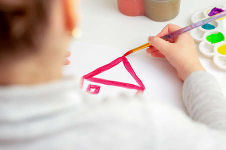 Child is drawing house roof with watercolors on white paper.の写真素材