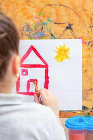 Child is drawing house with watercolors on the easel.の写真素材