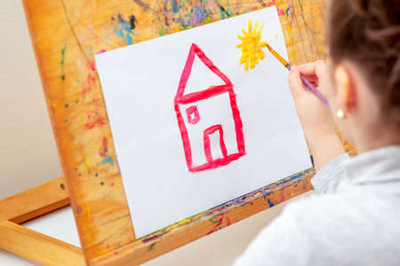 Child is drawing house with watercolors on the easel.の写真素材