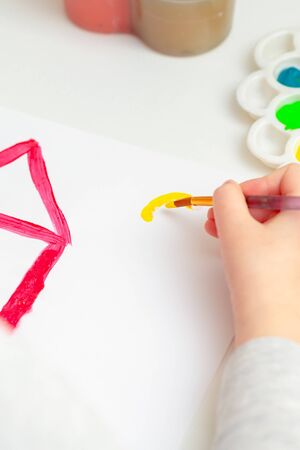 Close up of child's hand drawing with brush house and sun on white paper.の写真素材