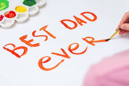 Close up of hand of child drawing handwritten text Best Dad Ever by watercolors on white paper. Father's Day and family concept.の写真素材