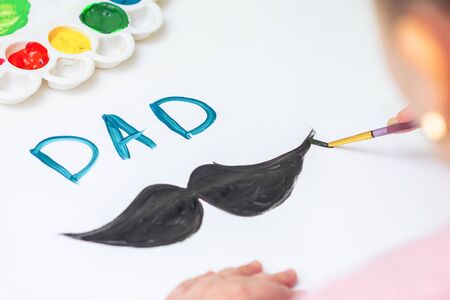 Close up of hand of child drawing black mustache with word Dad by watercolors on white paper. Father's Day and family concept.の写真素材