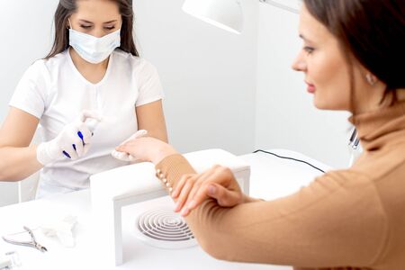 Manicurist is applying antiseptic on client's hands in manicure salon.の写真素材