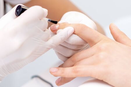 Manicure master hands covering clear varnish to female nail. Care nail fingers of hands.の写真素材