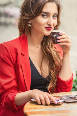 Portrait of young woman with cup drinking coffee at city street cafe.の写真素材