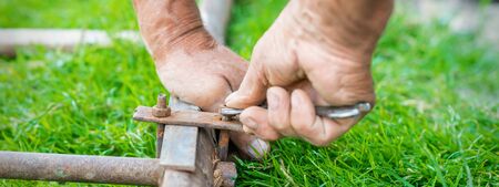 hand of an elderly man twisting the nut with a wrench outdoors. Repair by wrench.