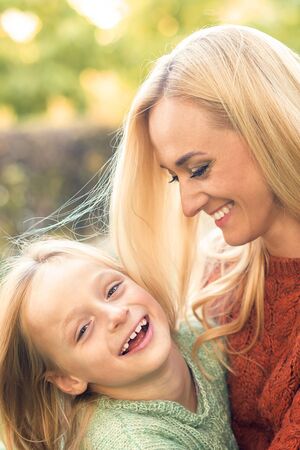 Beautiful young caucasian mother and little daughter smiling together on the green grass in the Autumn Parkの写真素材