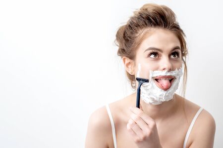 Beautiful young caucasian woman shaving her face by razor on white background. Pretty woman with...