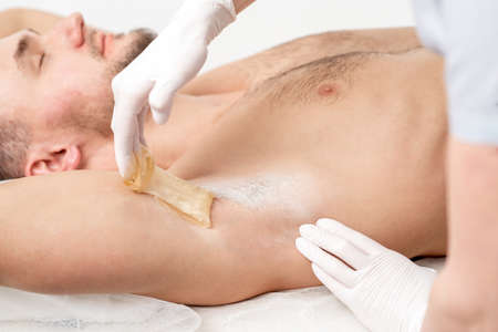 Depilation and epilation male armpit with liquid sugar paste. Hand of cosmetologist applying wax paste on armpit of man. Smooth underarm conceptの写真素材