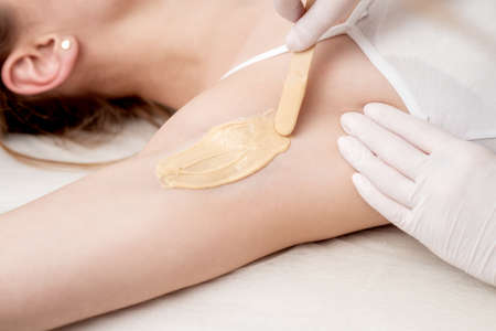 Depilation and epilation female armpit with liquid sugar paste by spatula. Hand of cosmetologist applying wax paste on armpit. Smooth underarm conceptの写真素材