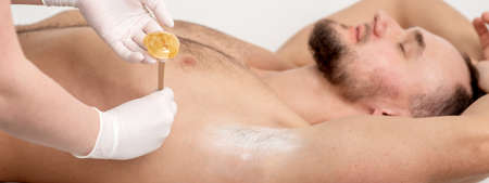 Depilation and epilation male armpit with liquid sugar paste by spatula. Hand of cosmetologist applying wax paste on armpit. Smooth underarm conceptの写真素材