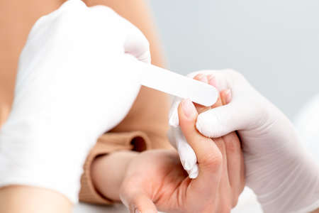 Young woman receiving a manicure by a beautician with nail file in a nail salon. Manicurist filing...