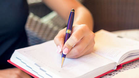 Woman hand is writing business plan on small notebook at outdoor area at cafe. Business concept.の写真素材