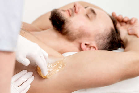 Depilation and epilation male armpit with liquid sugar paste. Hand of cosmetologist applying wax paste on armpit of man. Smooth underarm conceptの写真素材