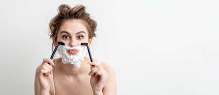 Beautiful young caucasian woman shaving her face by two razors on white background. Pretty woman...