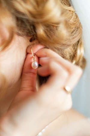 Beautiful caucasian young bride dresses earrings before wedding. Selective focusの写真素材