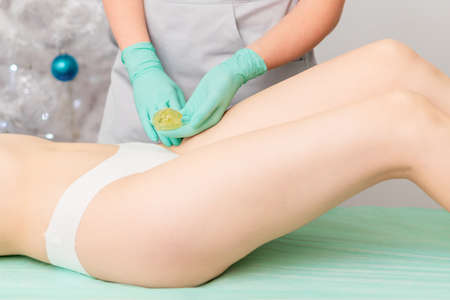 Beautician waxing legs of woman in spa center.